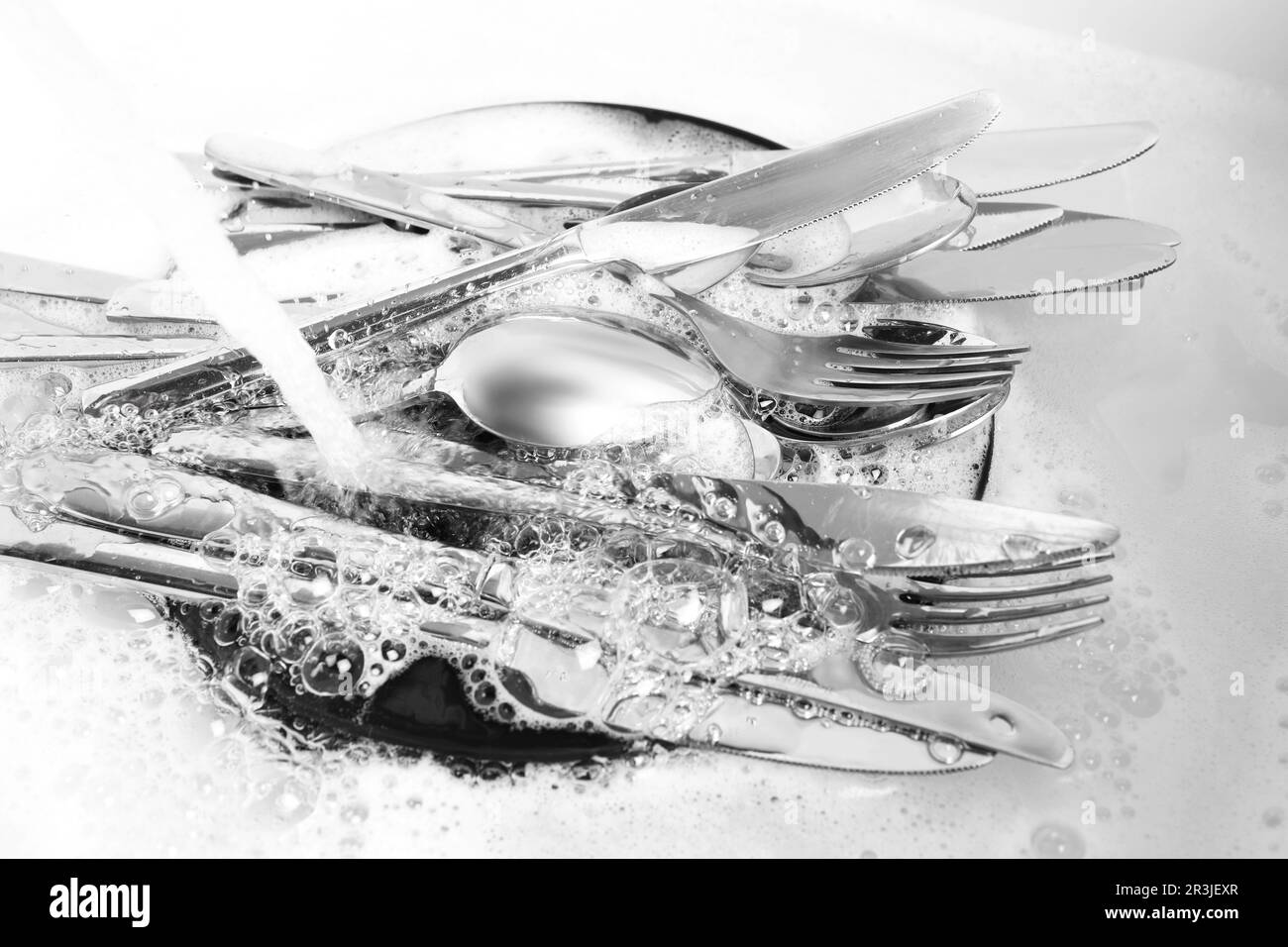 Washing silver spoons, forks and knives under stream of water in kitchen sink, closeup Stock
