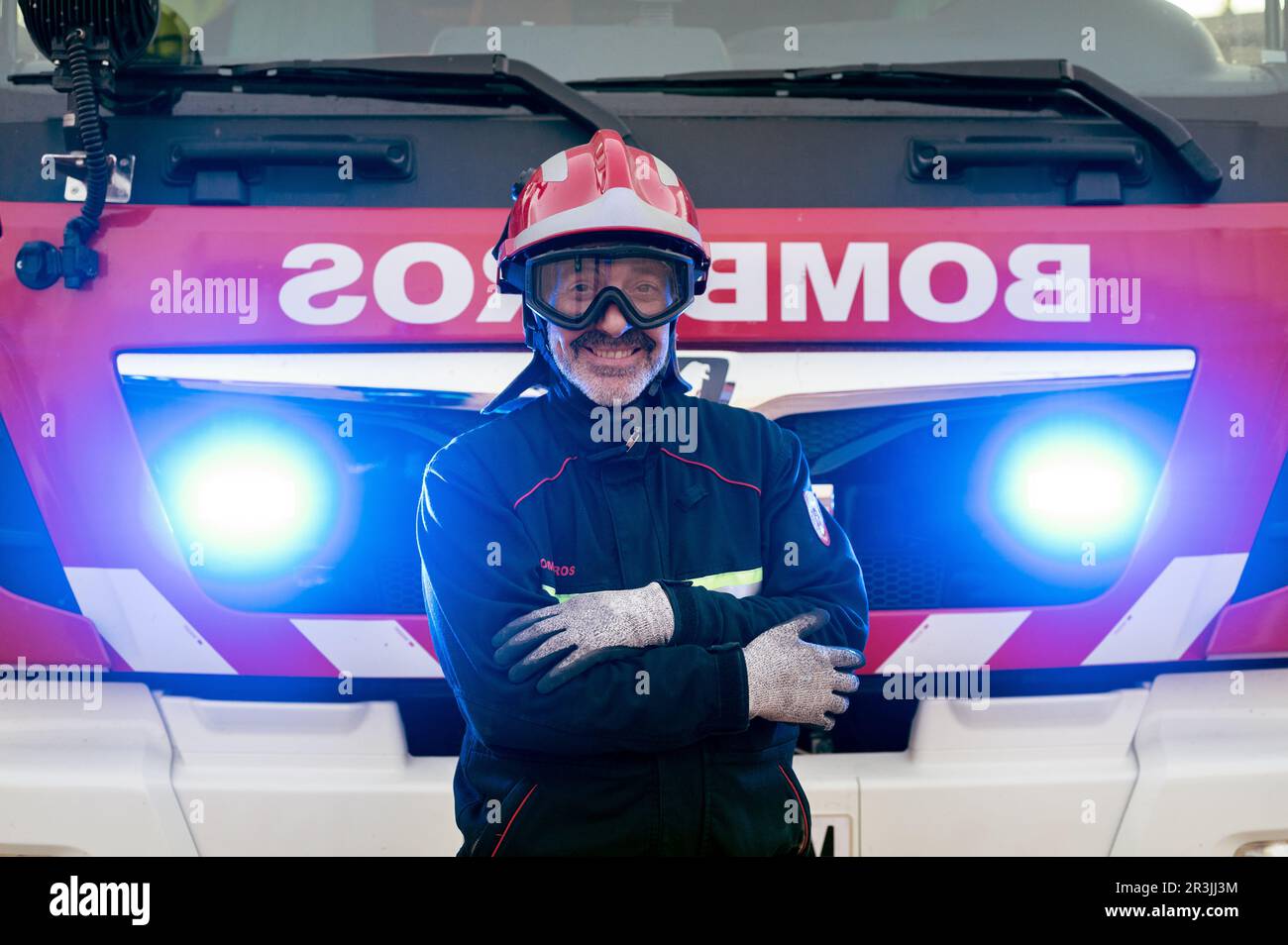 Firefighter posing in front of a fire truck with his arms crossed. High quality photography. Stock Photo