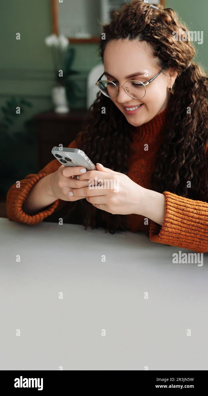 Young smiling woman wearing glasses holding a smartphone using cellphone modern technology, looking at mobile, checking cell phone apps, texting, and Stock Photo