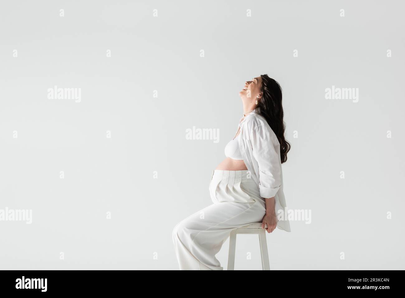 side view of joyful expecting mother with wavy brunette hair sitting on