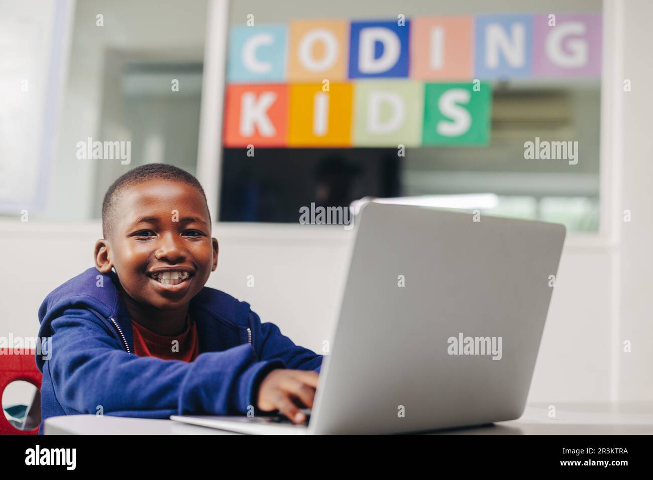 Excited young boy smiling at the camera as he sits with a laptop in a ...