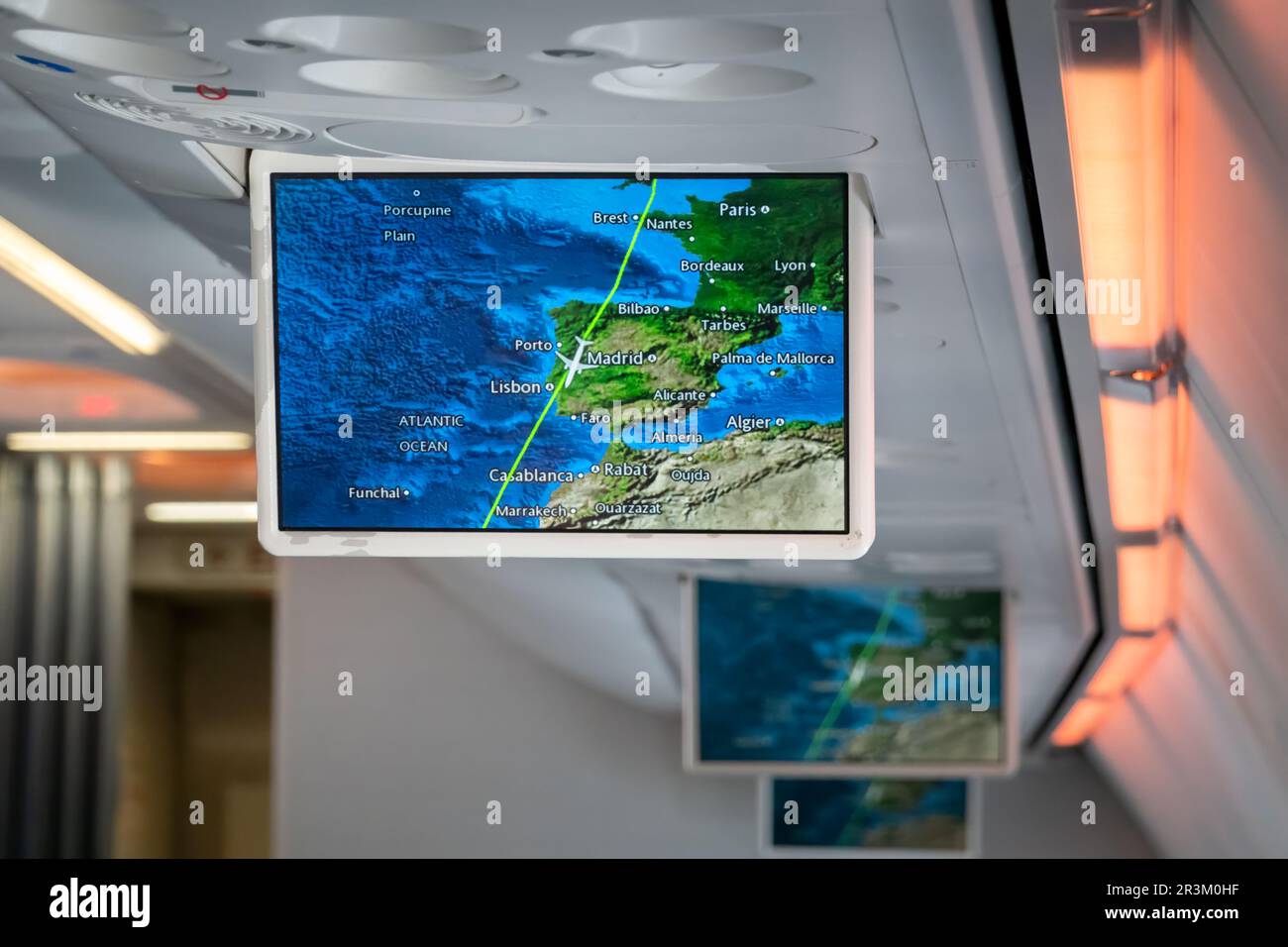 A drop down screen in an passenger aircraft cabin displays flight information for passengers with the panes current position shown on a map Stock Photo