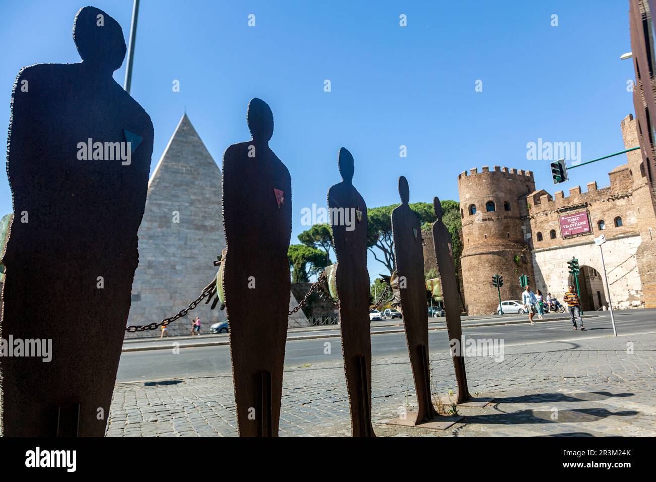 Metal statues of men and women stand in a plaza in front of a castle ...