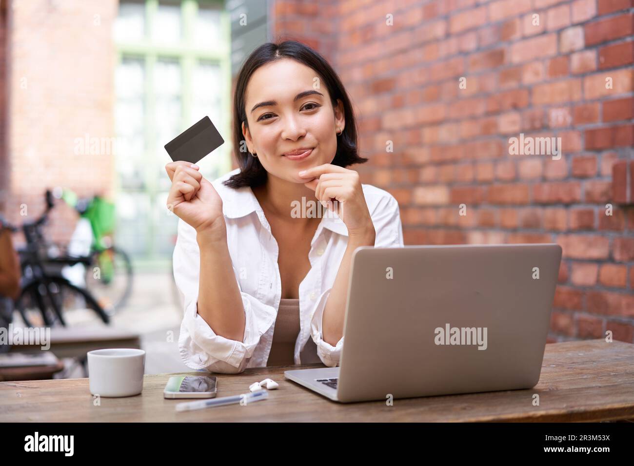 Stylish young asian woman doing shopping online, sitting with credit card and laptop, buying in internet and paying contactless, Stock Photo