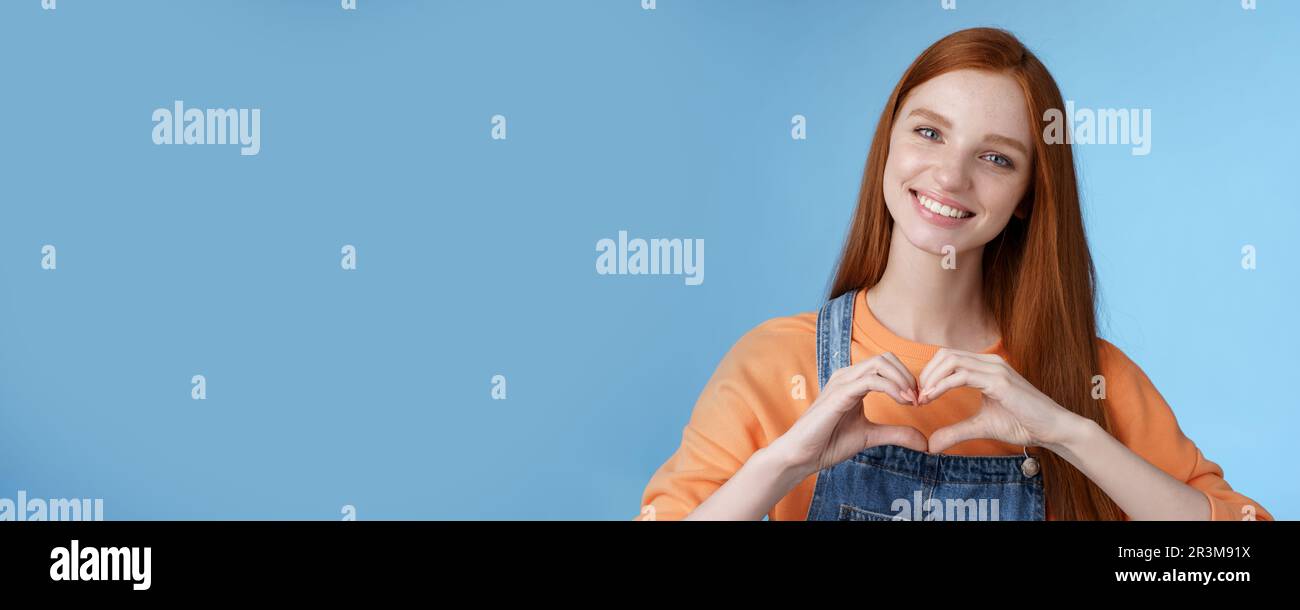Love you. Attractive romantic tender redhead smiling gentle girlfriend blue eyes freckles show heart chest express sympathy roma Stock Photo