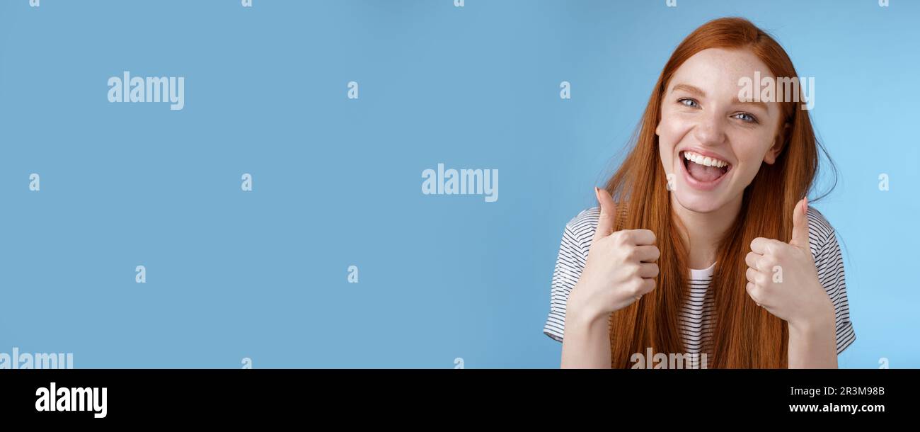 Enthusiastic amused outgoing redhead beautiful girl say yeah supportive like awesome idea show thumbs-up approval recommend gest Stock Photo