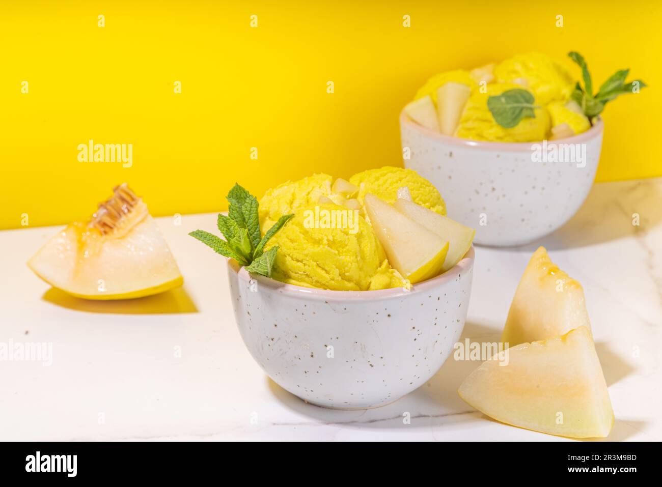 Homemade melon ice cream balls in portioned bowls, with slices of fresh