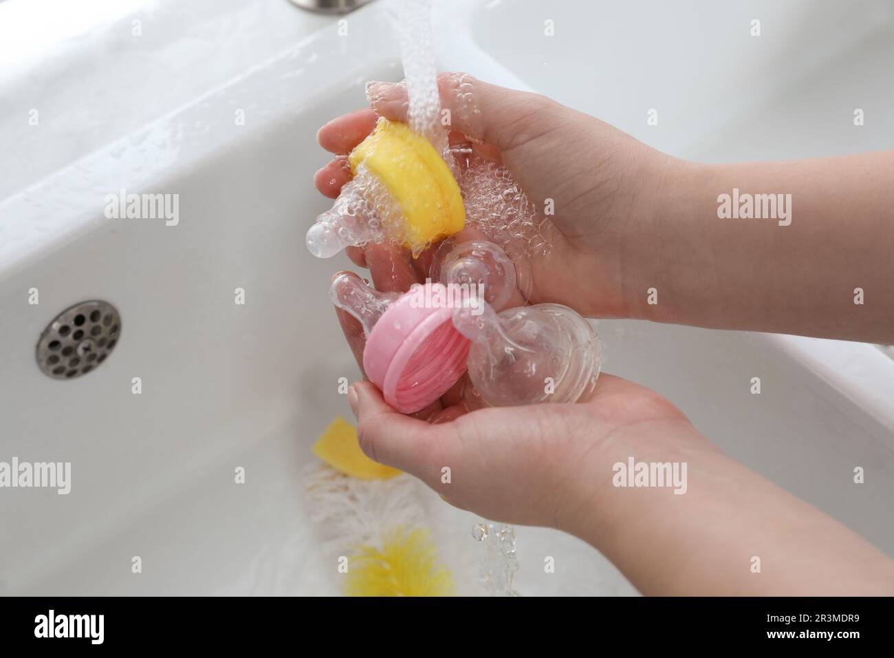 Woman washing baby bottle nipples under stream of water, above