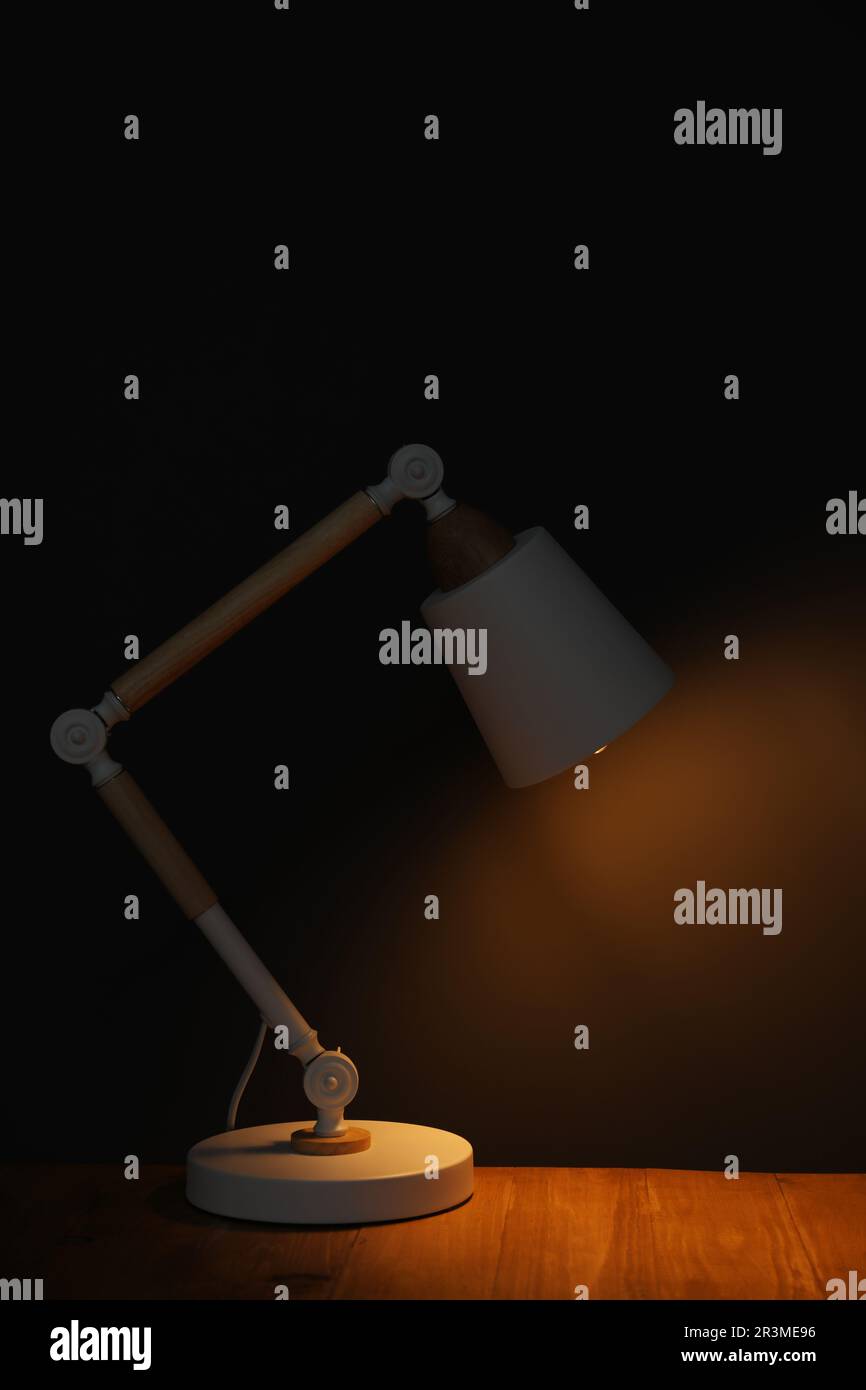 Stylish modern desk lamp on wooden table at night Stock Photo