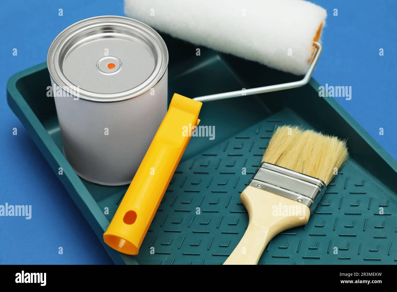 Can of orange paint, brush, roller and container on blue background