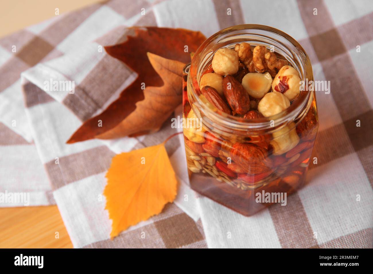 Different nuts with honey in jar and dry leaves on wooden table