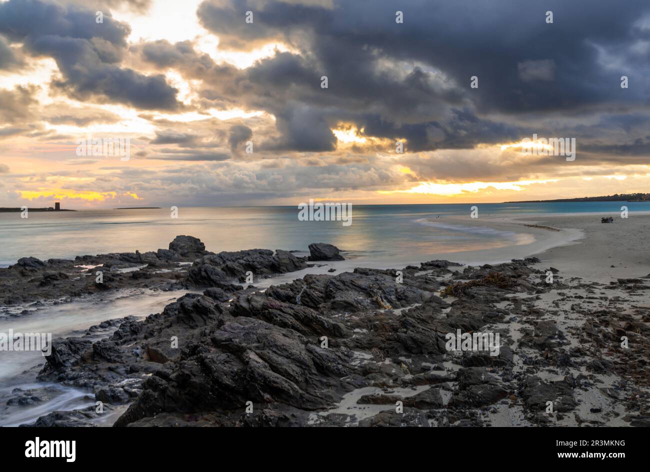 View of La Pelosa beach in Sardinia at sunrise with rocky reef in the foreground Stock Photo
