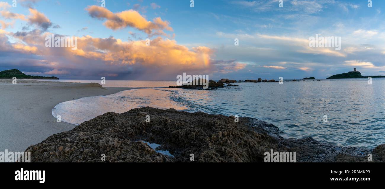 A panorama view of a colorful sunset at Nora Beach in Sardinia with the Coltellazzo Tower in the background Stock Photo