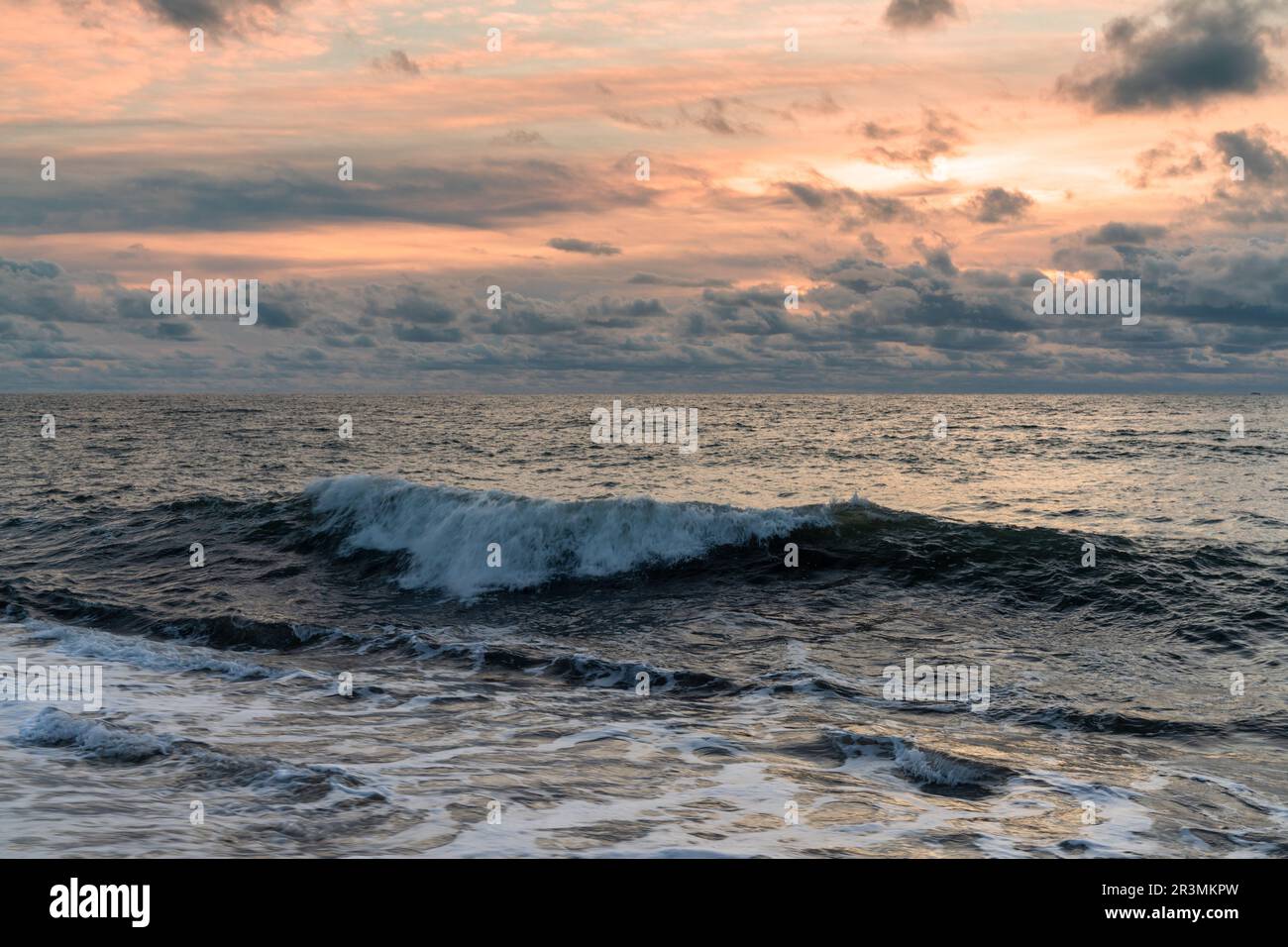 Background landscape of a large wave breaking and rolling to shore under a stormy sunset sky Stock Photo