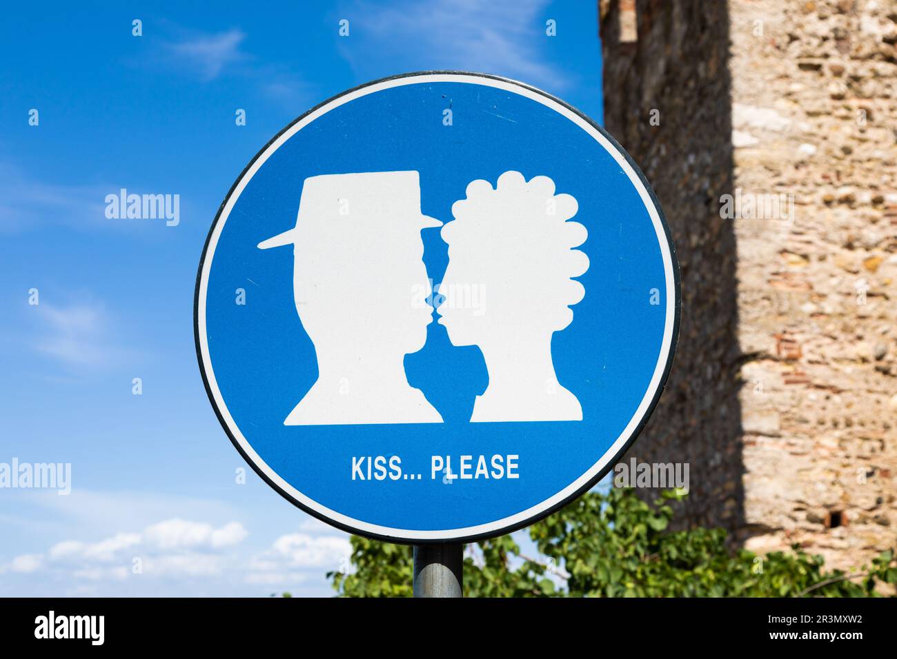 Kiss street sign located in public area in front of Sirmione castle, Italy. Concept of love, couple, romantic. Stock Photo