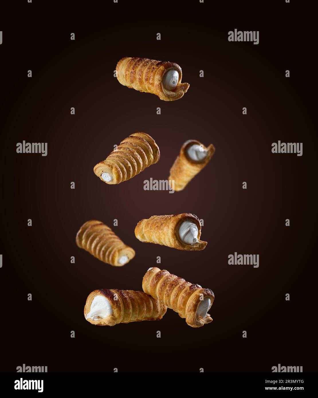 Baked crispy tubes with whipped protein cream levitate on a brown background Stock Photo