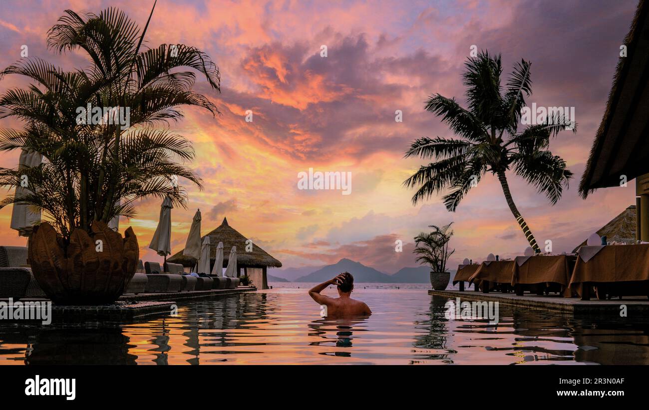 Luxury swimming pool tropical resort, holidays Seychelles, Young man during sunset by swimpool Stock Photo