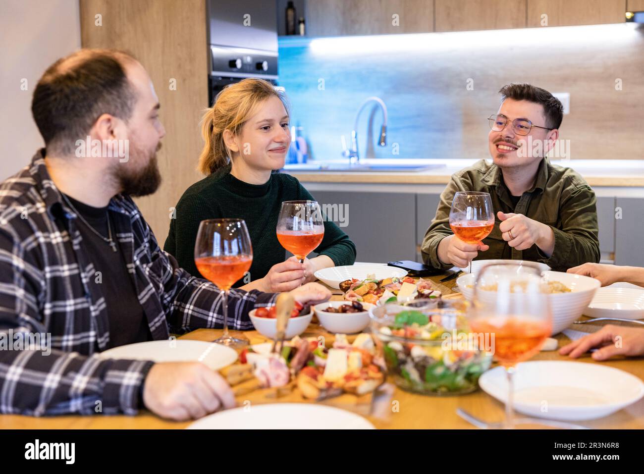 Group of friends having dinner at home, enjoying a good laugh in cozy setting. Stock Photo