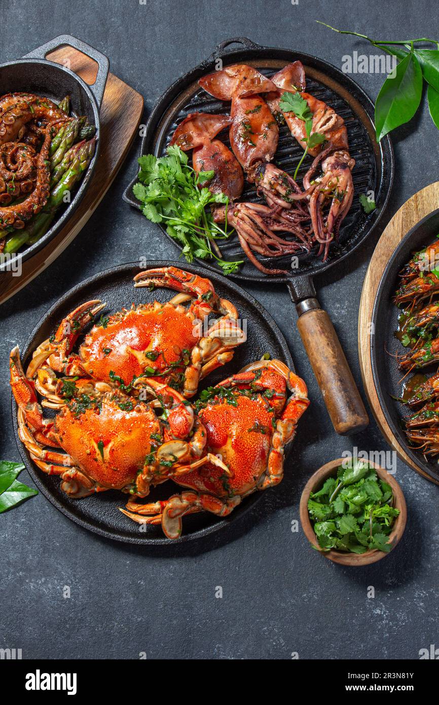https://c8.alamy.com/comp/2R3N81Y/set-of-seafood-dishes-crabs-octopus-squids-and-tiger-shrimps-on-cast-iron-pans-and-plates-on-a-black-background-top-view-2R3N81Y.jpg