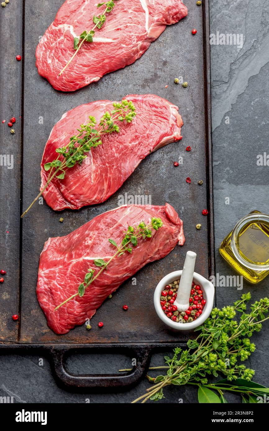 Raw beef steaks with herbs and spices on cast iron frying board, top