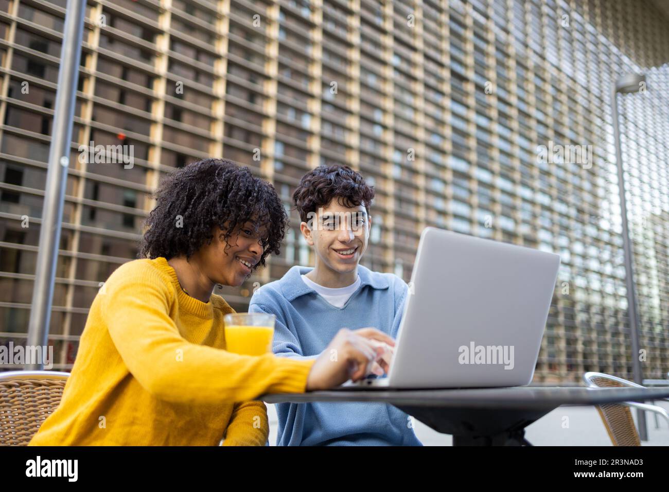 Young multiracial male and female friends smiling and looking at laptop while sitting in daylight Stock Photo