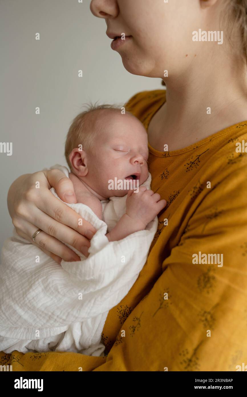 Side view cute newborn child in white swaddle lying on lap of crop