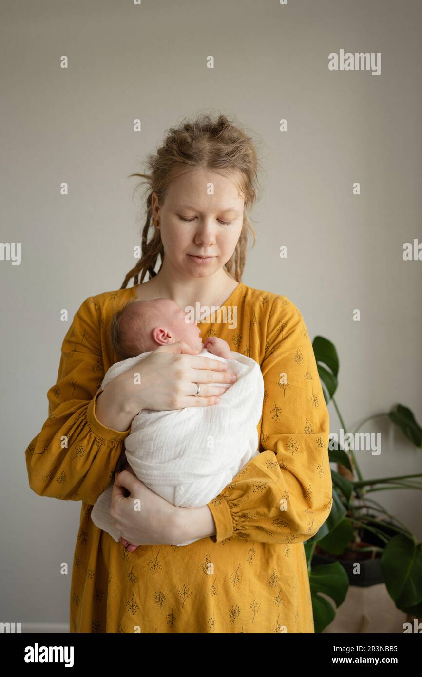 Cute newborn child in white swaddle lying on lap of crop female Stock Photo