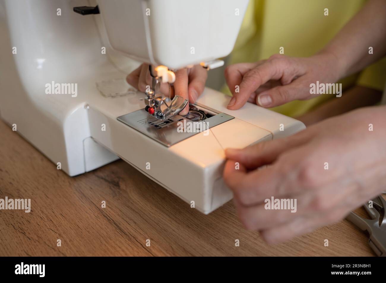 Anonymous female dressmakers putting thread into sewing machine while