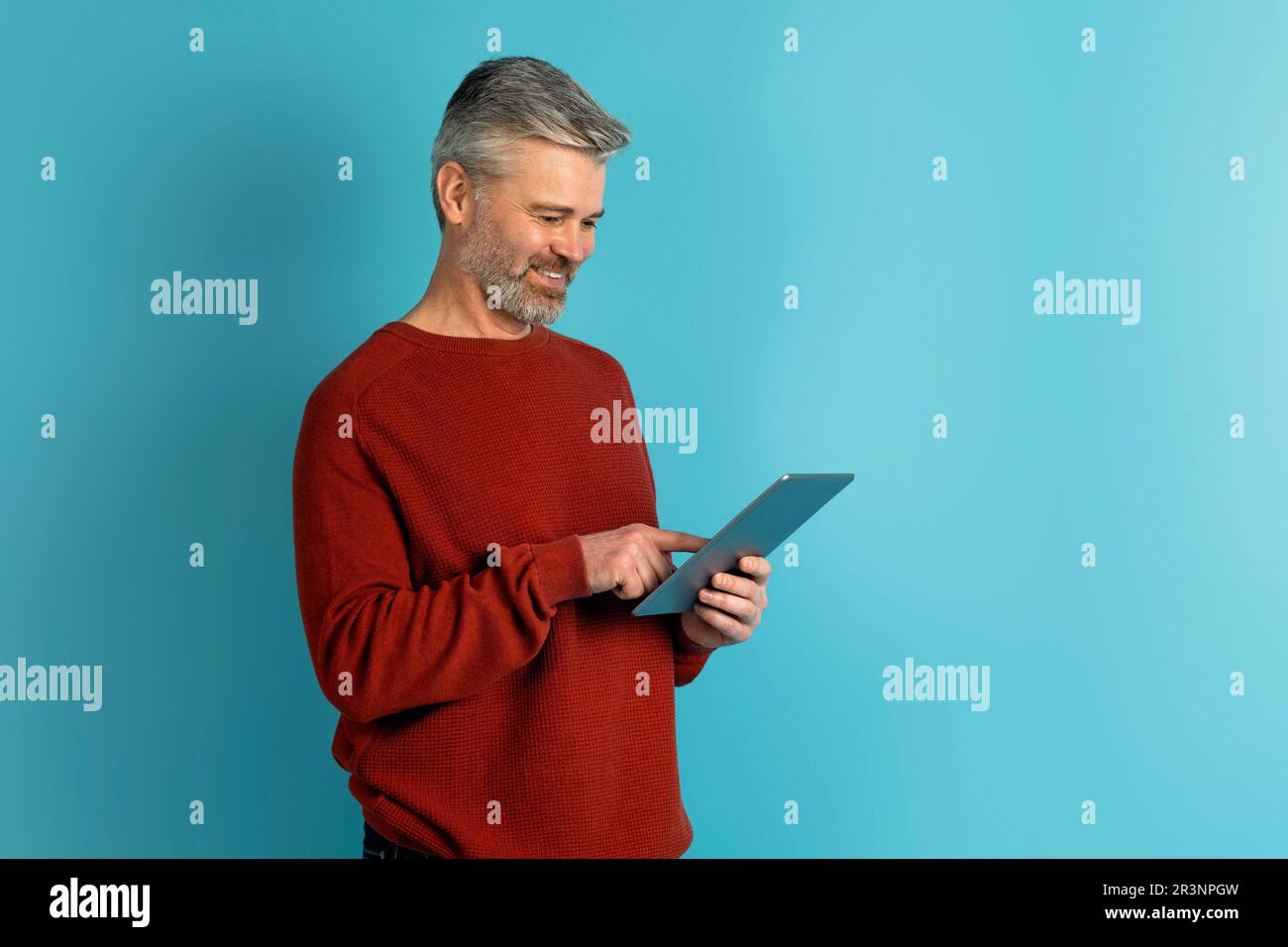 Joyful middle aged man using digital tablet on blue Stock Photo
