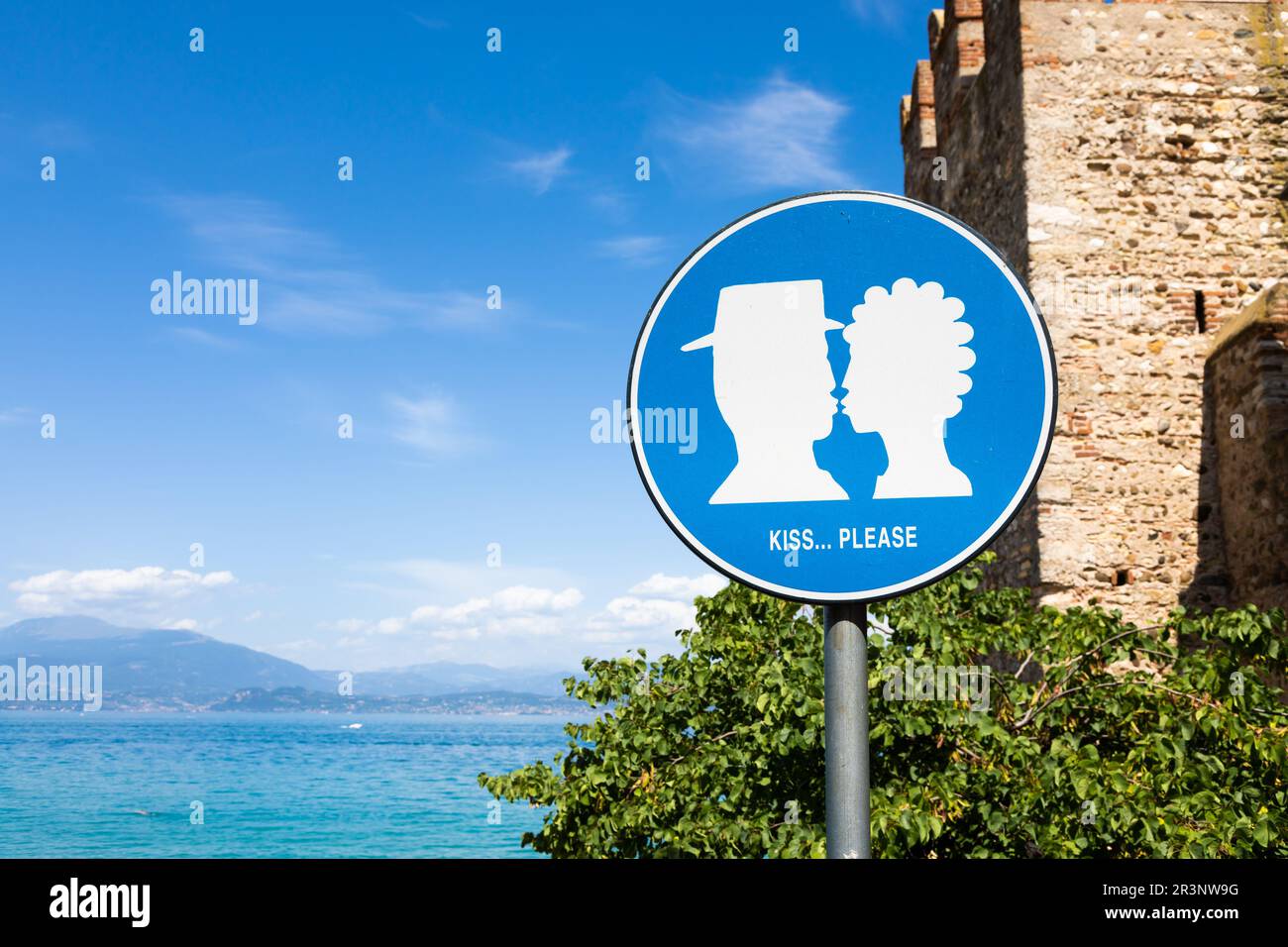 Kiss street sign located in public area in front of Sirmione castle, Italy. Concept of love, couple, romantic. Stock Photo