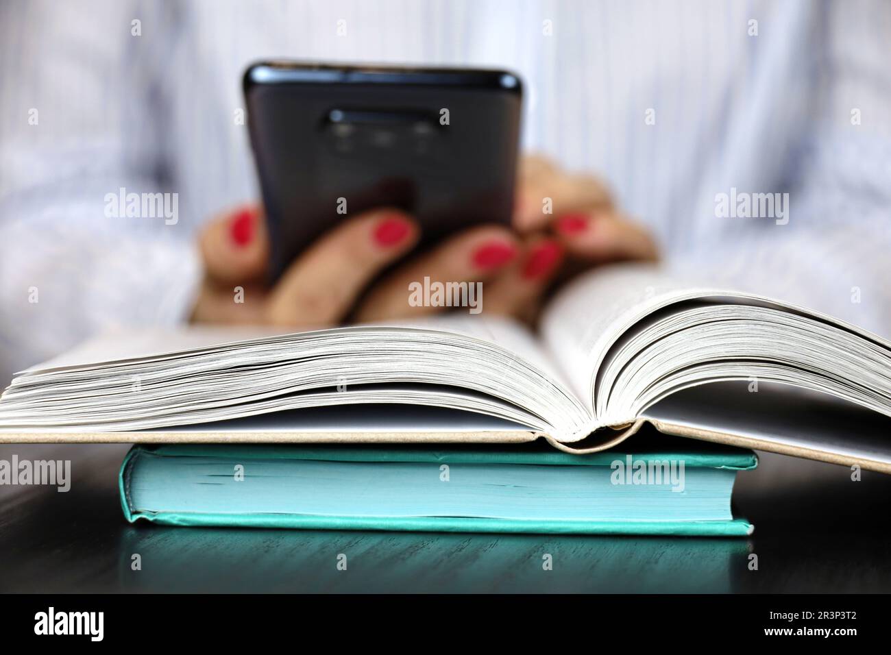 Woman reading a book while sitting at table with smartphone in hands. Concept of education and literature Stock Photo