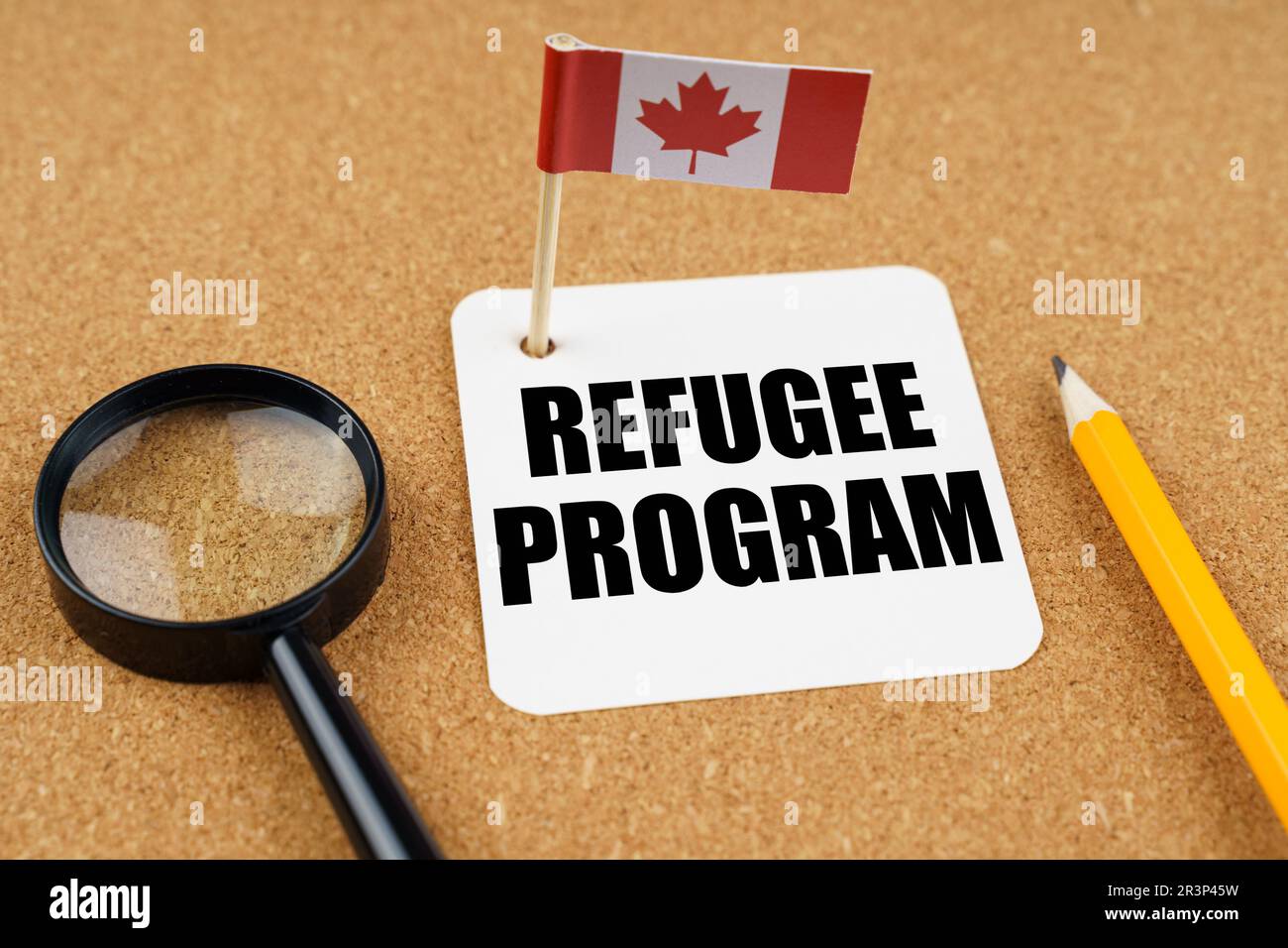 On the table is the flag of Canada, a pencil, a magnifying glass and a sheet of paper with the inscription - Refugee Program Stock Photo