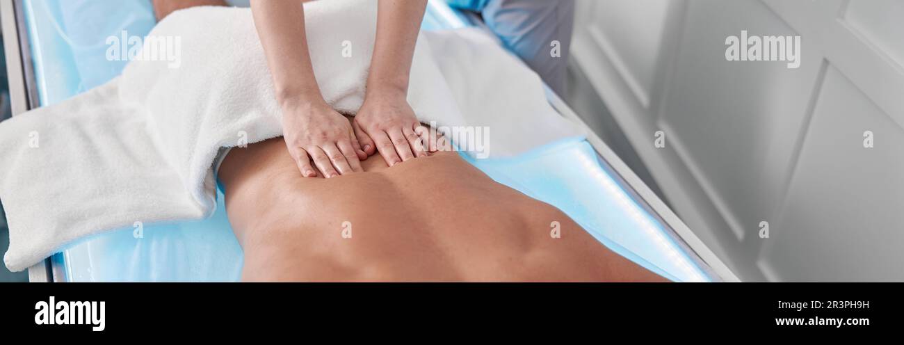 Relaxed male patient undergoes procedure of back massage lying in glowing couch Stock Photo