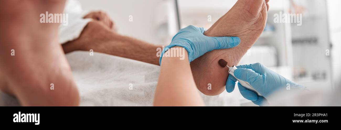 Careful podiatrist grinds heel of male client with modern tool at pedicure procedure in salon Stock Photo
