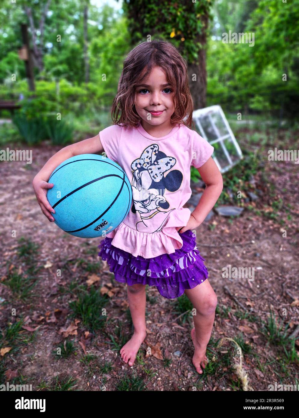 Little girl posing for the camera outside with a basketball. The background is blurred behind her (NC State, 2023) Stock Photo