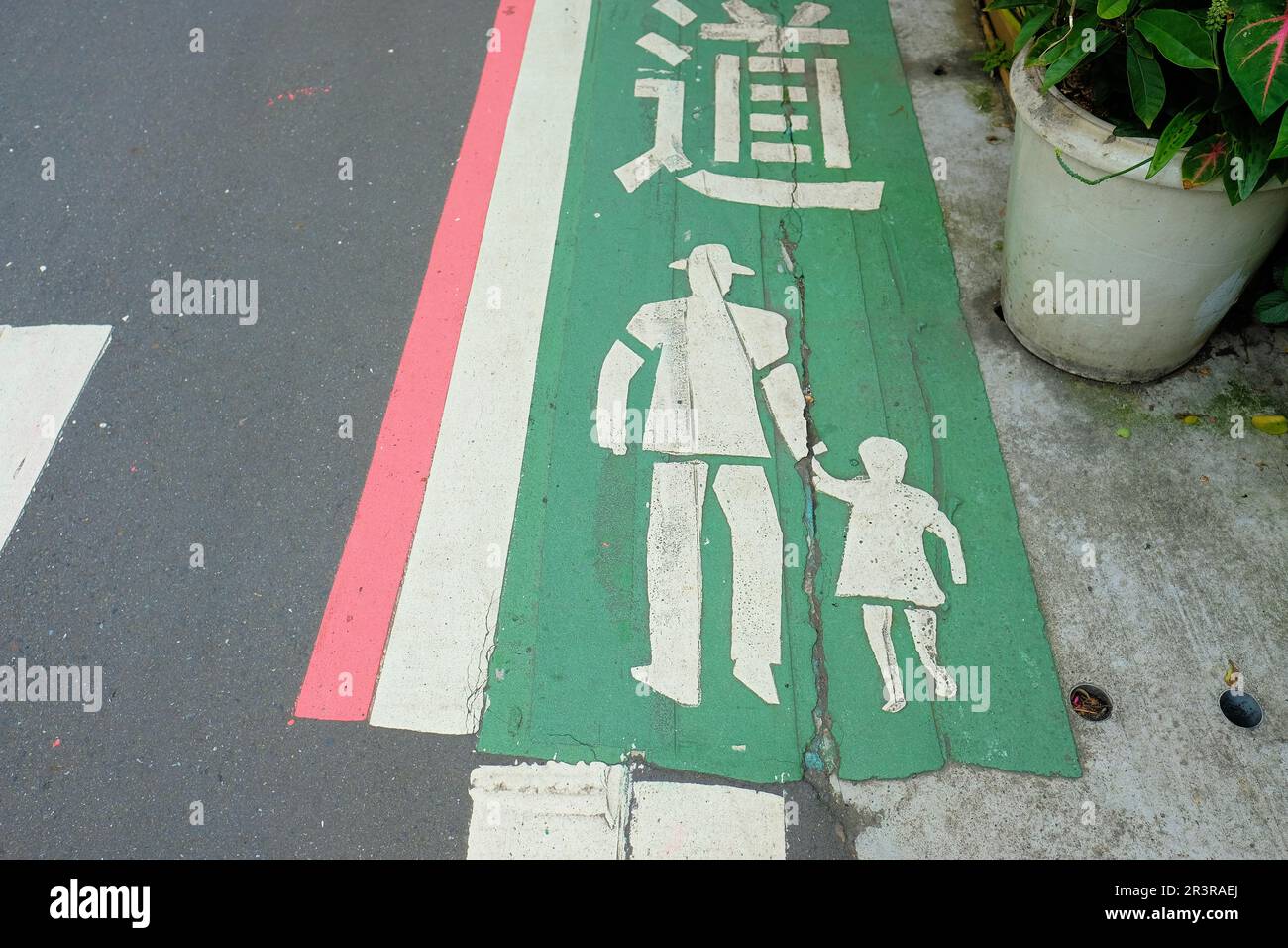 White silhouette of man holding a child's hand on a designated green path on the street for pedestrians and pedestrian traffic; Taipei, Taiwan. Stock Photo