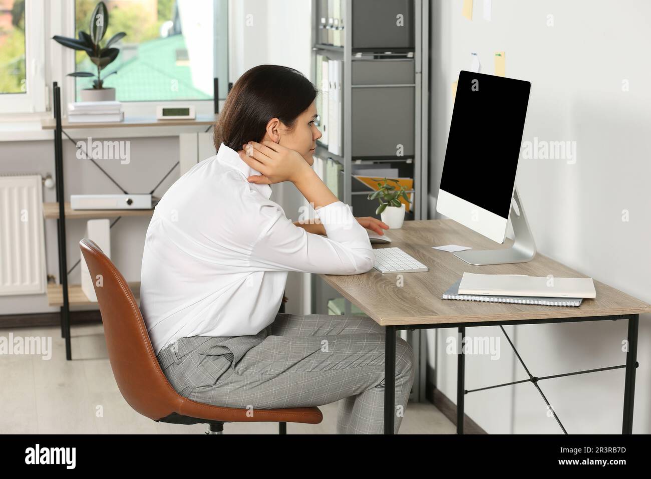 Young woman with bad posture sitting at workplace in office. Symptom of scoliosis Stock Photo