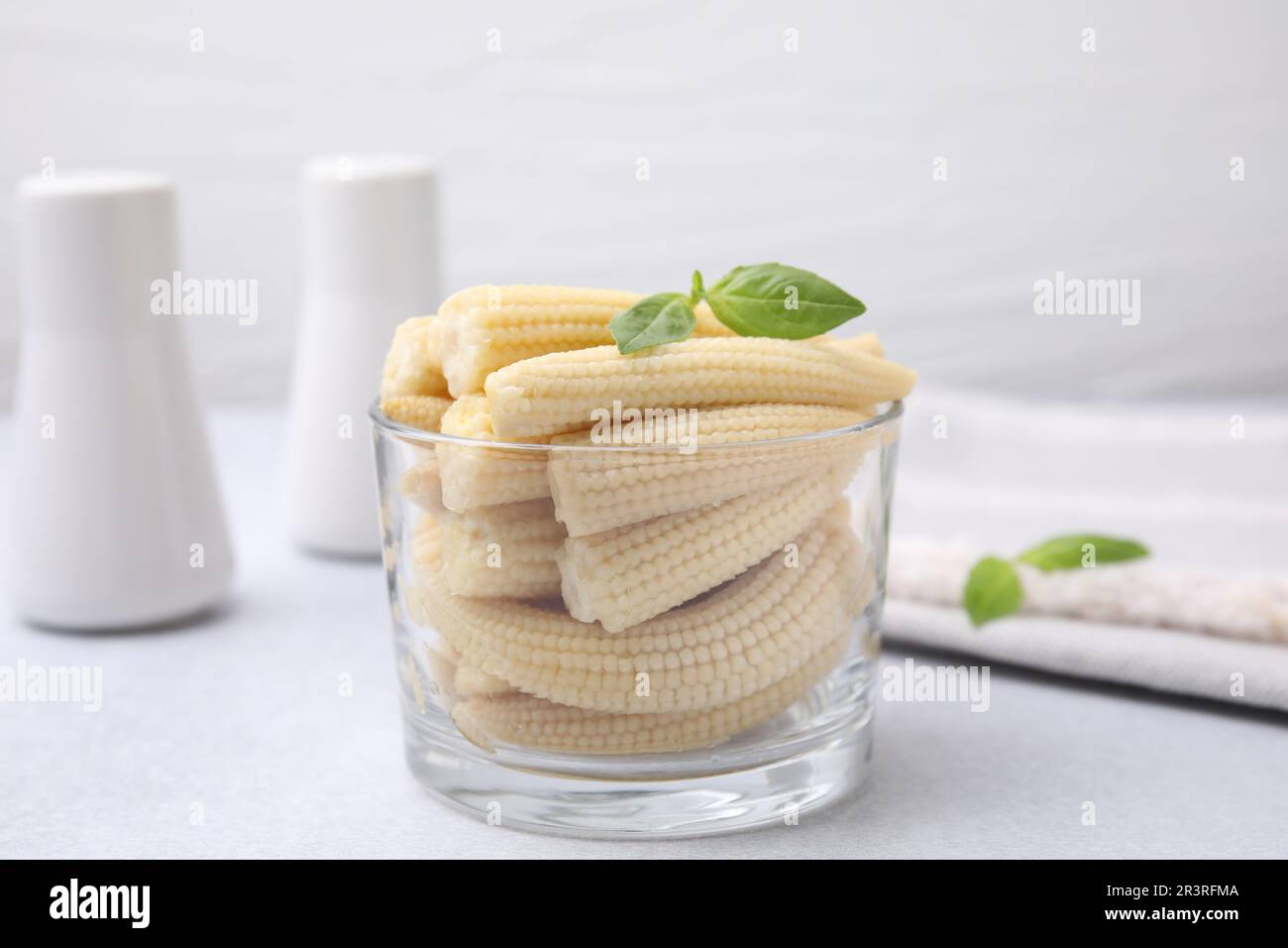 Canned baby corns with basil on white table, closeup Stock Photo