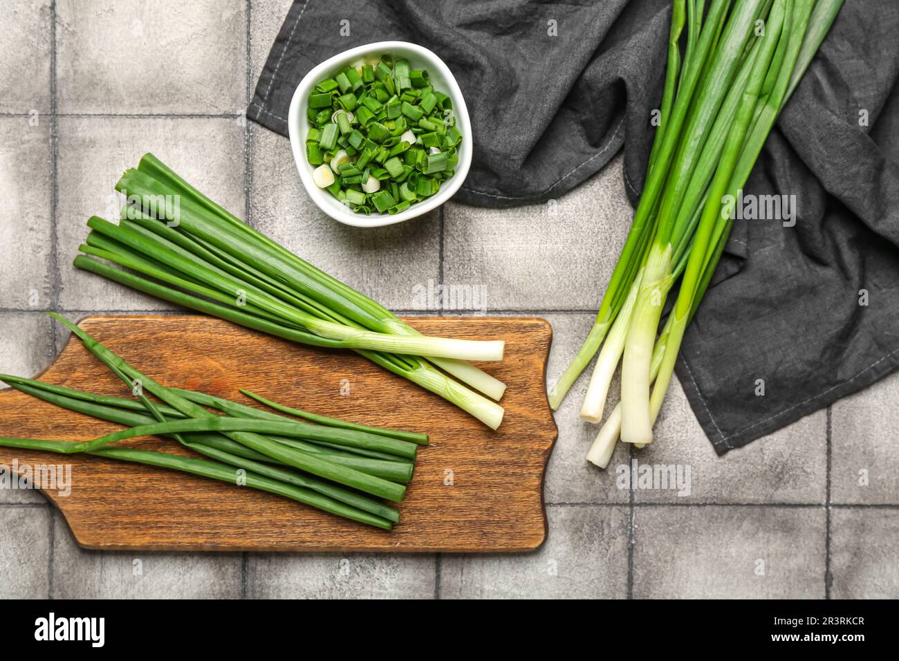 Wooden board and bowl with fresh green onion on dark tile background ...