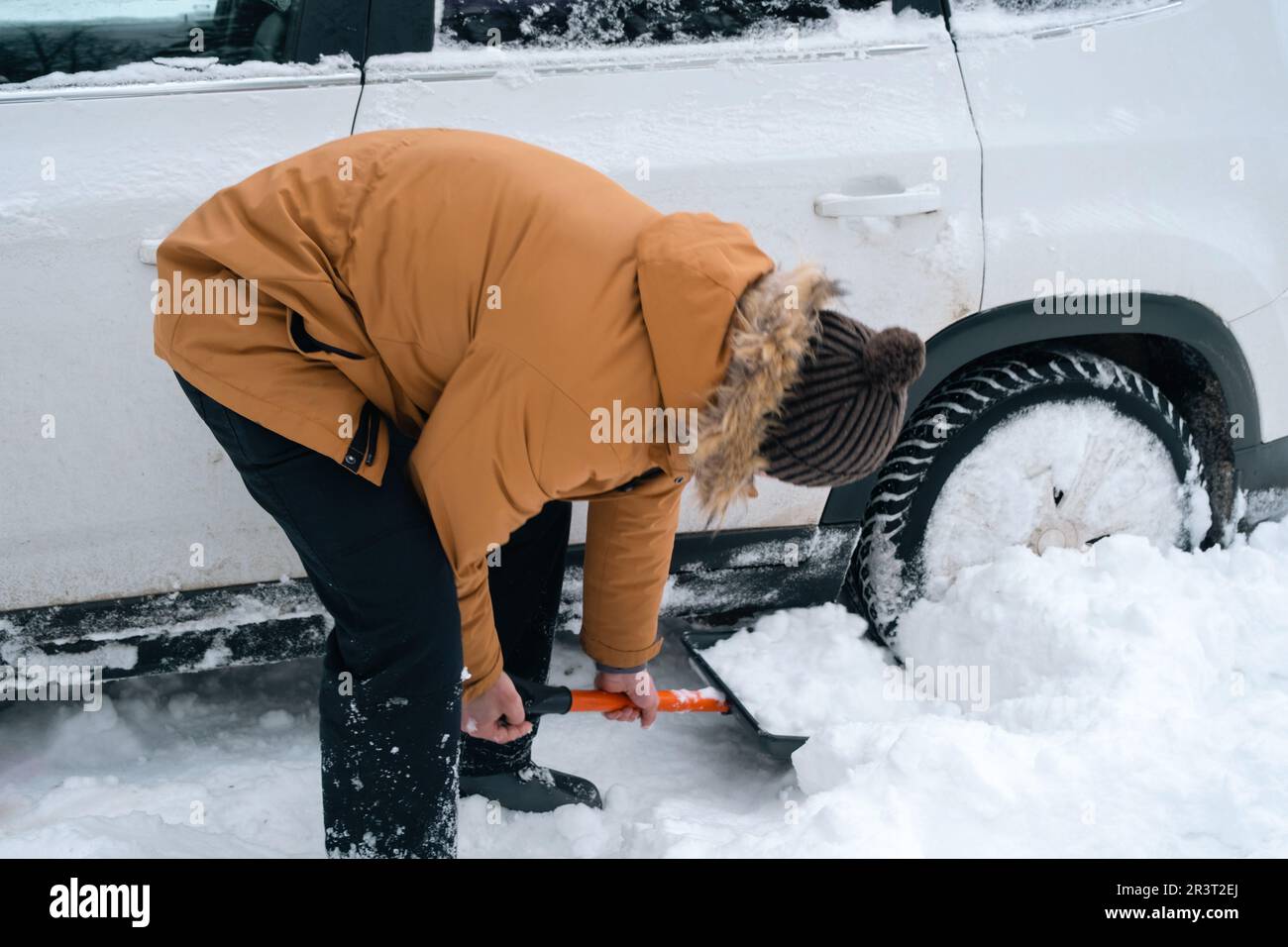 A man digs out a stalled car in the snow with a car shovel. Transport in winter got stuck in a snowdrift after a snowfall, sat o Stock Photo