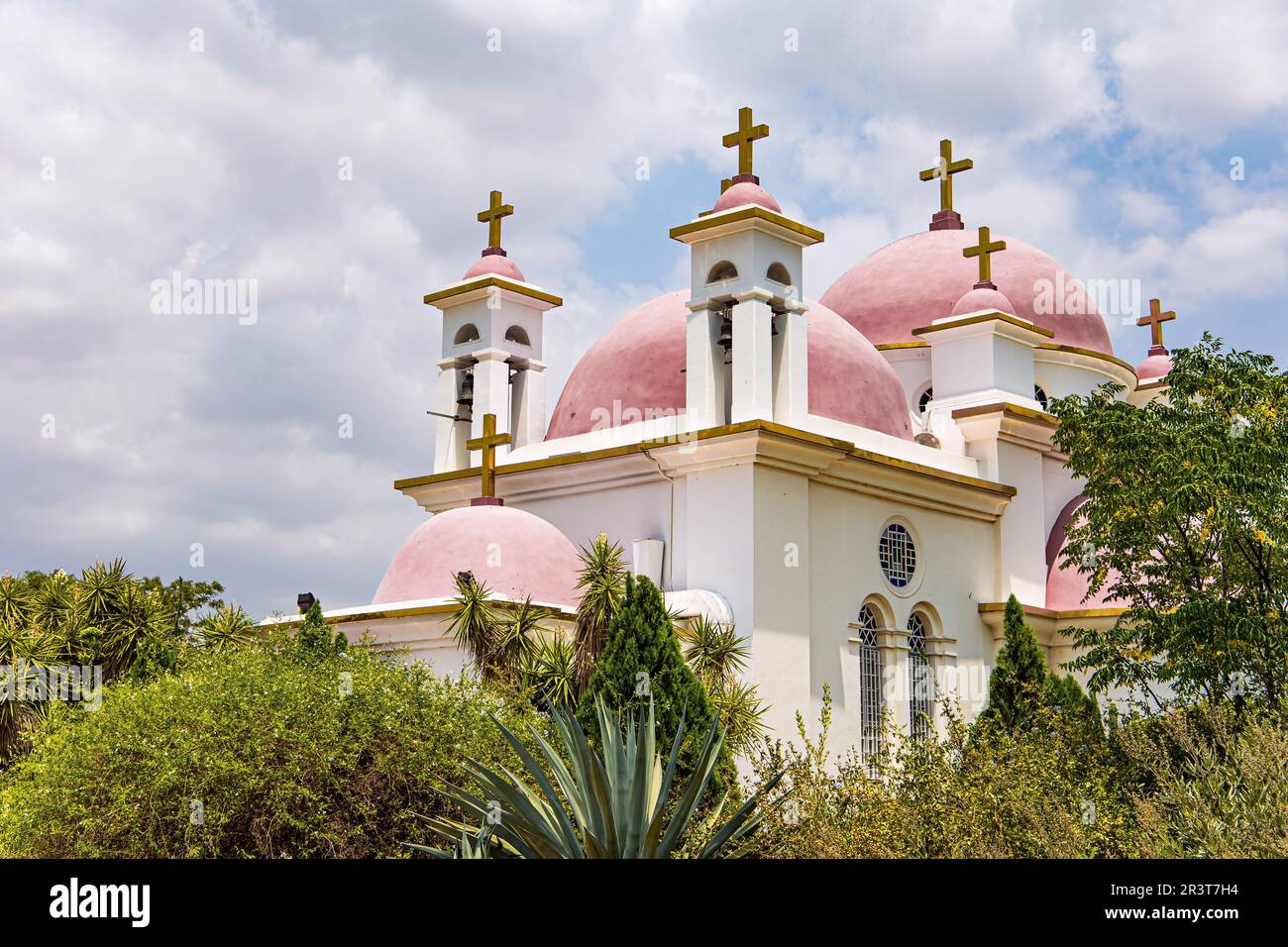 Greek Orthodox monastery of the Twelve Apostles. Capernaum. Israel. Tropical park around the Church. Pink domes with golden crosses of the monastery o Stock Photo