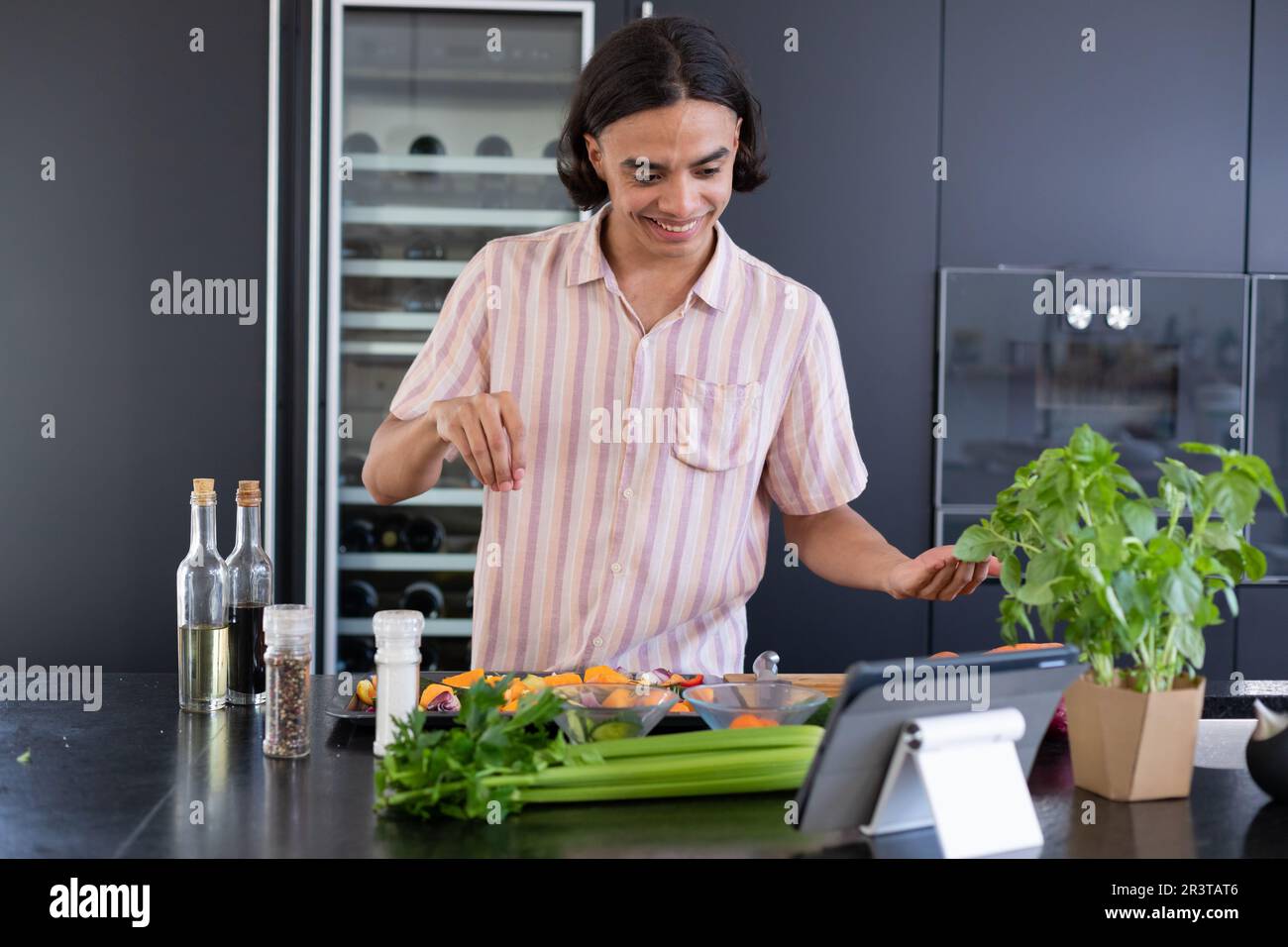 Happy biracial man cooking and using tablet in kitchen Stock Photo