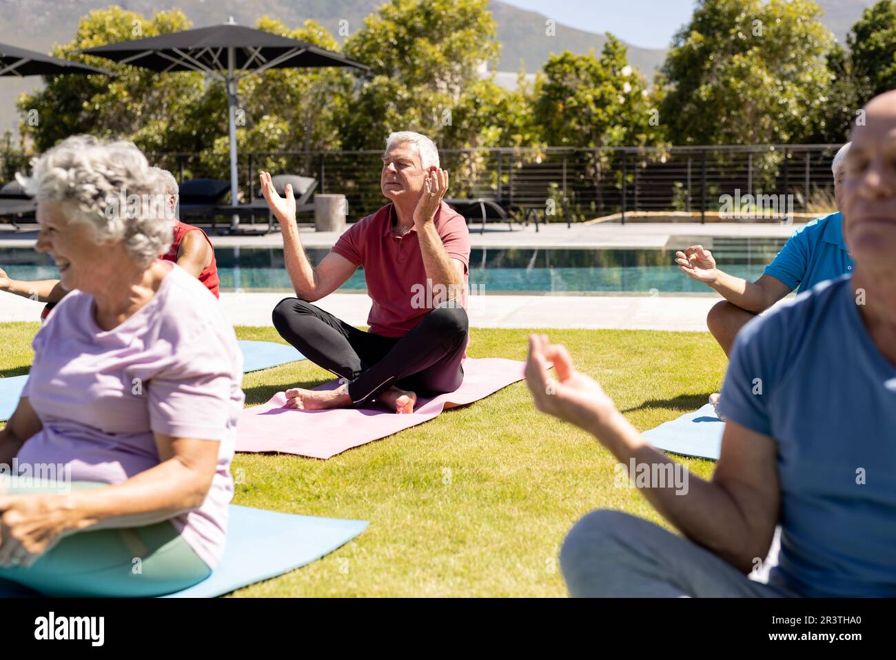 Happy diverse senior friends practicing yoga meditation sitting in sunny garden Stock Photo