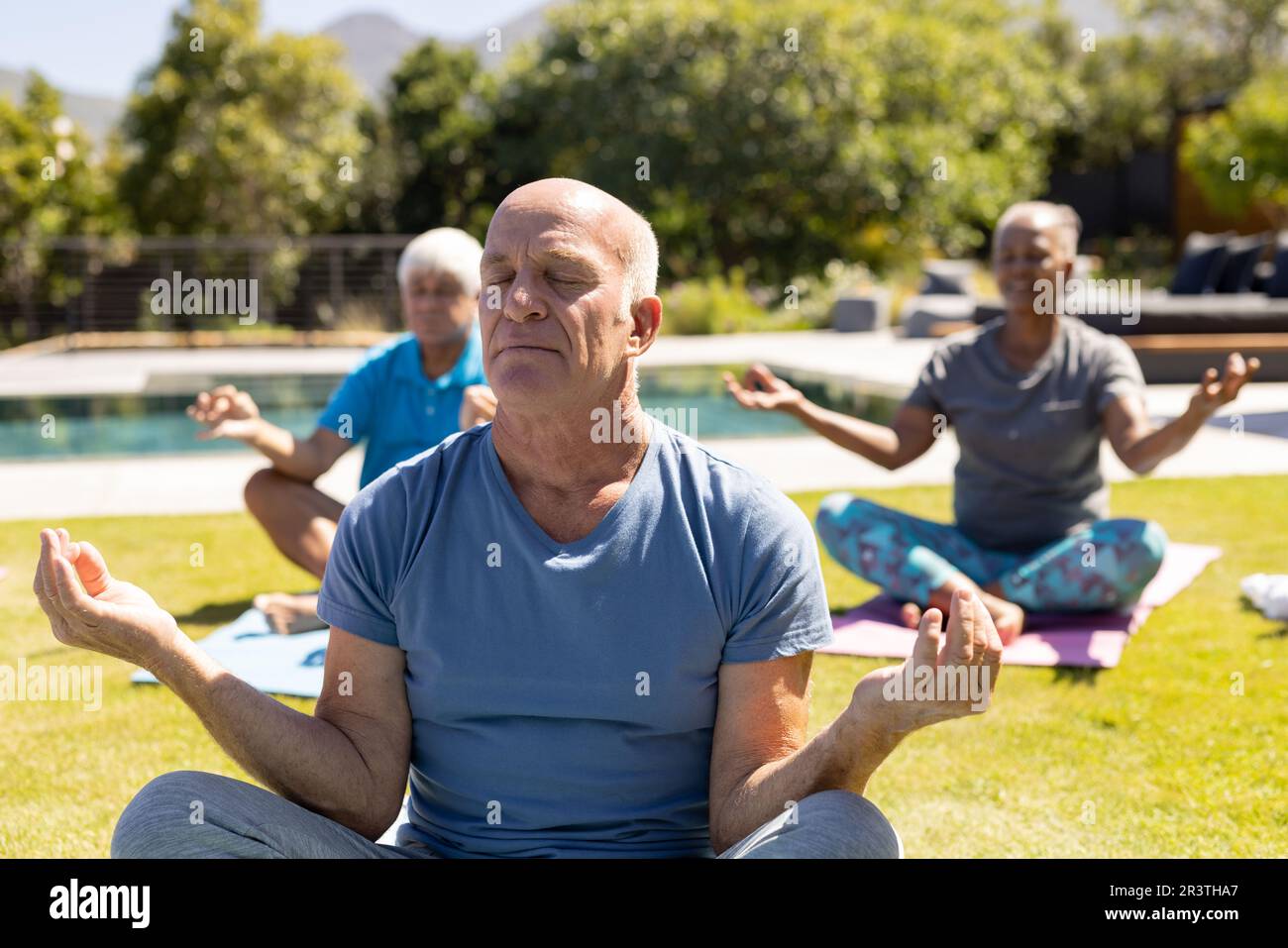 Happy diverse senior friends practicing yoga meditation sitting in sunny garden Stock Photo