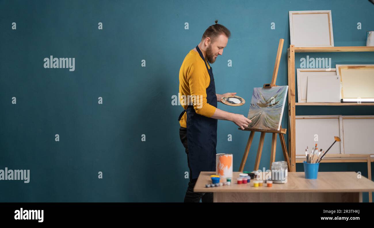 Young man painting on easel with brush in artist studio. Male artist ...