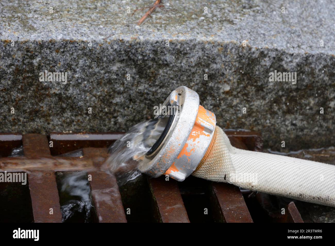 Water flowing from a tube into a street drain Stock Photo