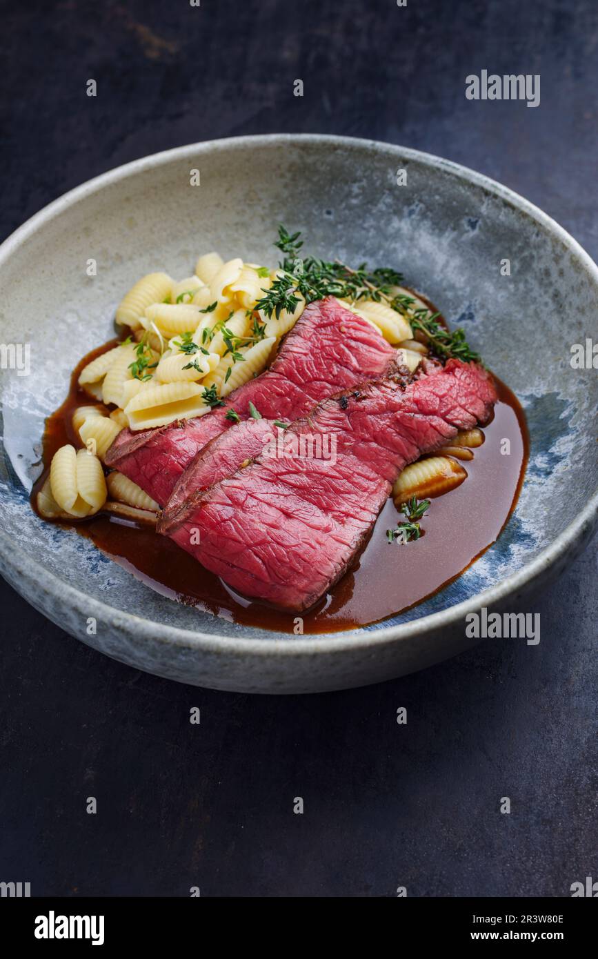 Traditional Italian chianina sliced roast beef with gnocchetti sardi pasta in spicy red wine sauce served as close-up in a Nordi Stock Photo