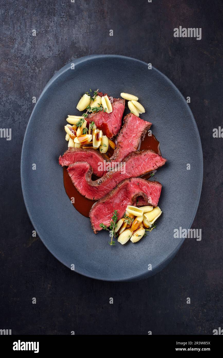 Traditional Italian chianina sliced roast beef with gnocchetti sardi pasta in spicy red wine sauce served as top view in a desig Stock Photo