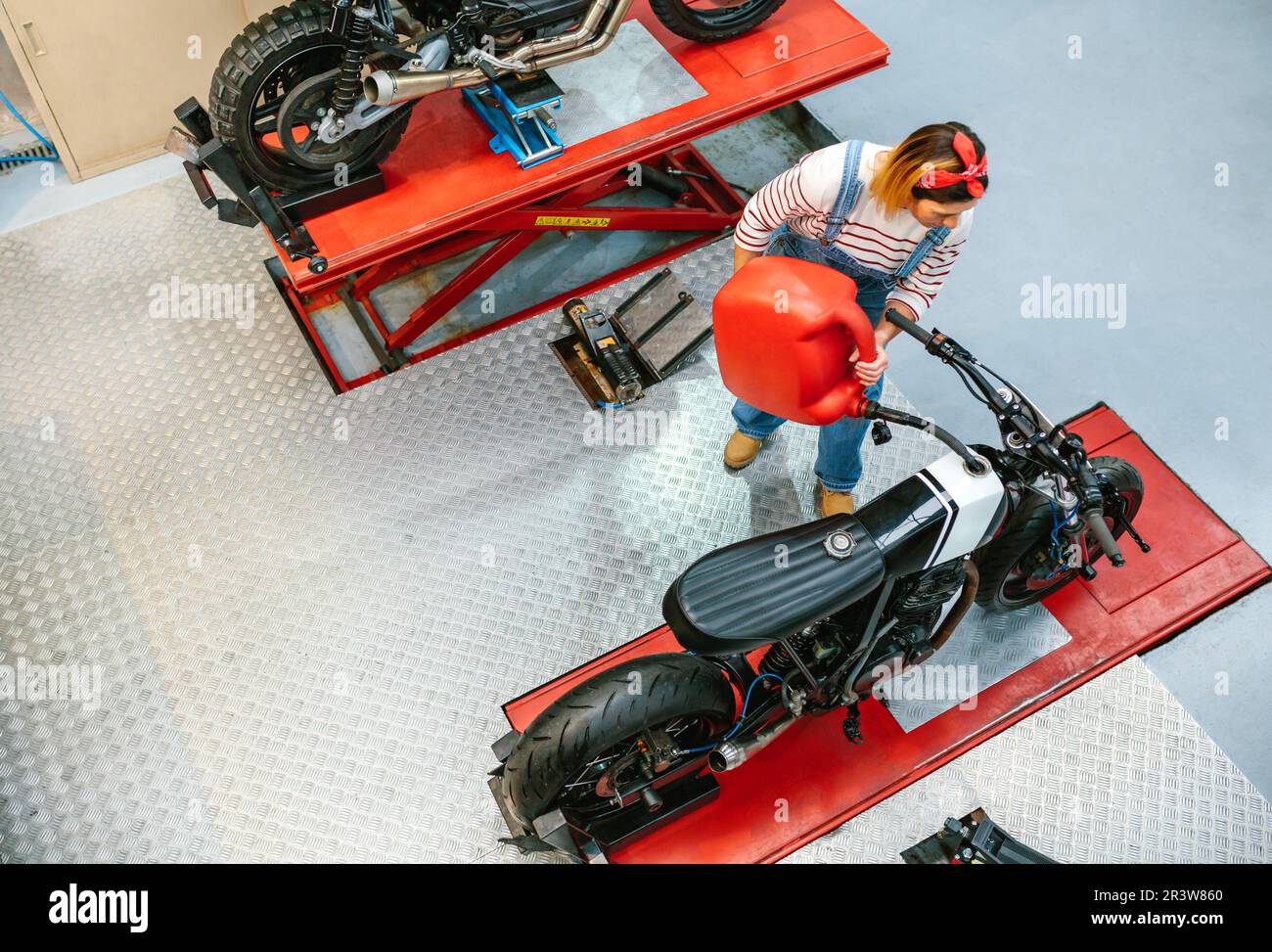 Mechanic woman with jerry can filling fuel tank of motorcycle on