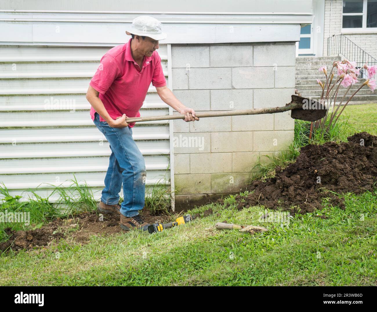 Man digging up soil using shovel on the side of garage wall, trying to exposure outside wall to find the leak into the garage. Stock Photo